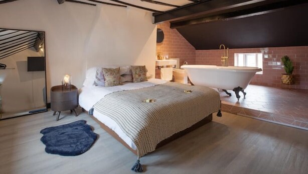 A bedroom with a large bed, a bathtub, and a mirror. - The Cottage (Poulton-le-Fylde)