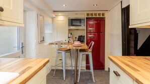 A compact kitchen with white cabinets, a red refrigerator, and two bar stools. - The Cottage (Poulton-le-Fylde)