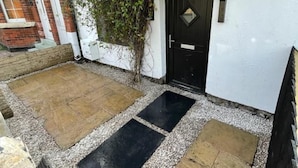 A courtyard with a black door, white walls, and a brick building in the background. - The Cottage (Poulton-le-Fylde)