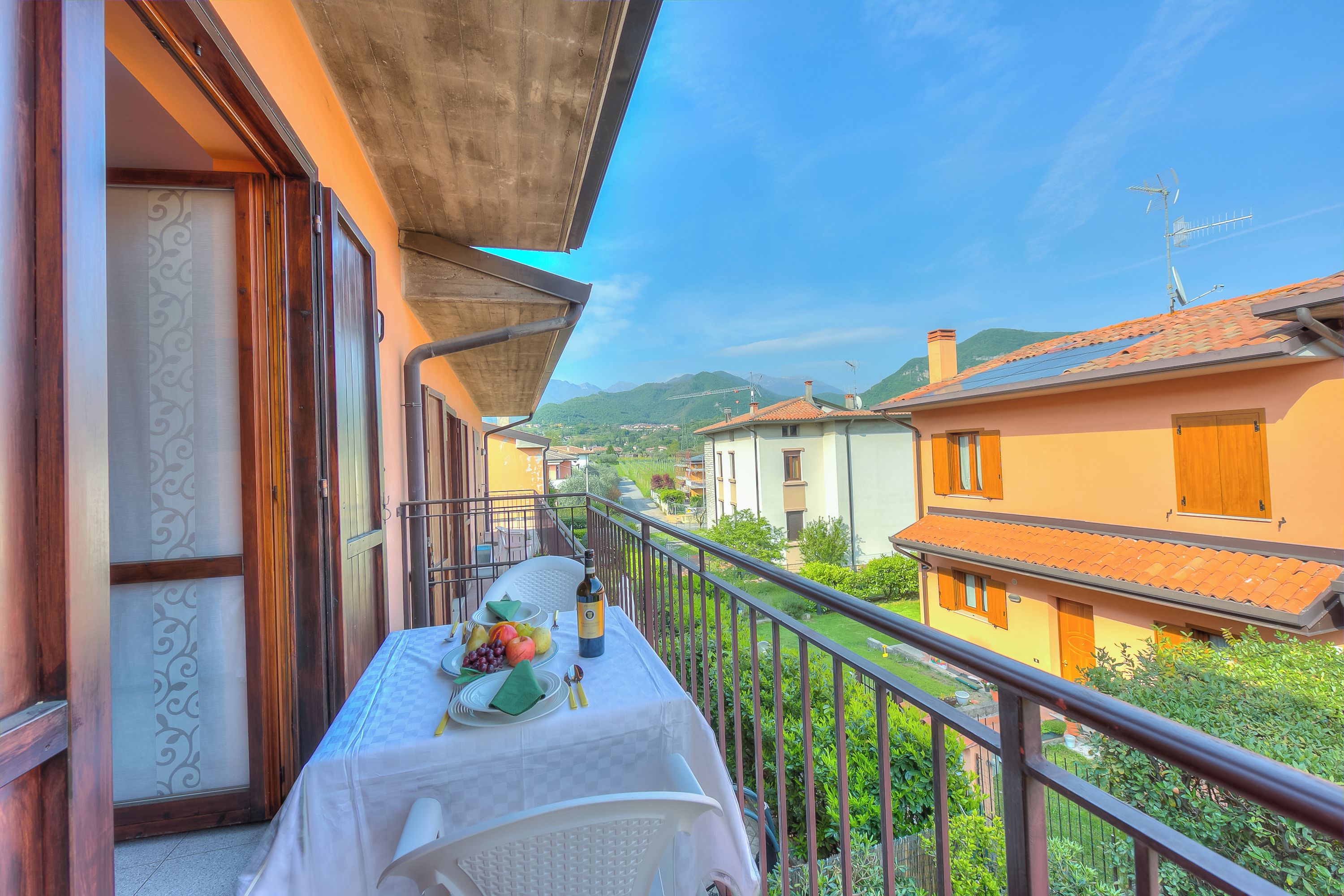 A balcony with a table set for a meal, overlooking a residential area with houses and mountains.