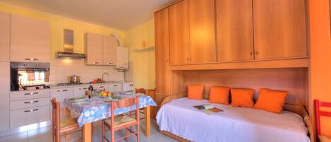 Une cuisine compacte avec une table à manger, des chaises et un lit agrémenté d’oreillers orange.