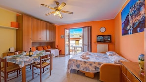 A room with a dining table set, two beds with floral bedding, a ceiling fan, and a view through an open door. - Peter's Cozy Studio-balcony+free Parking (Roe Volciano)