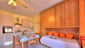 A compact kitchen with a dining table, chairs, and a bed with orange pillows. - Peter's Cozy Studio-balcony+free Parking (Roe Volciano)