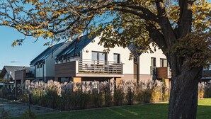A modern house with a balcony, surrounded by a well-maintained lawn and tall grasses.