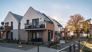 A modern two-story residential building with a balcony, a satellite dish, and a small garden area.