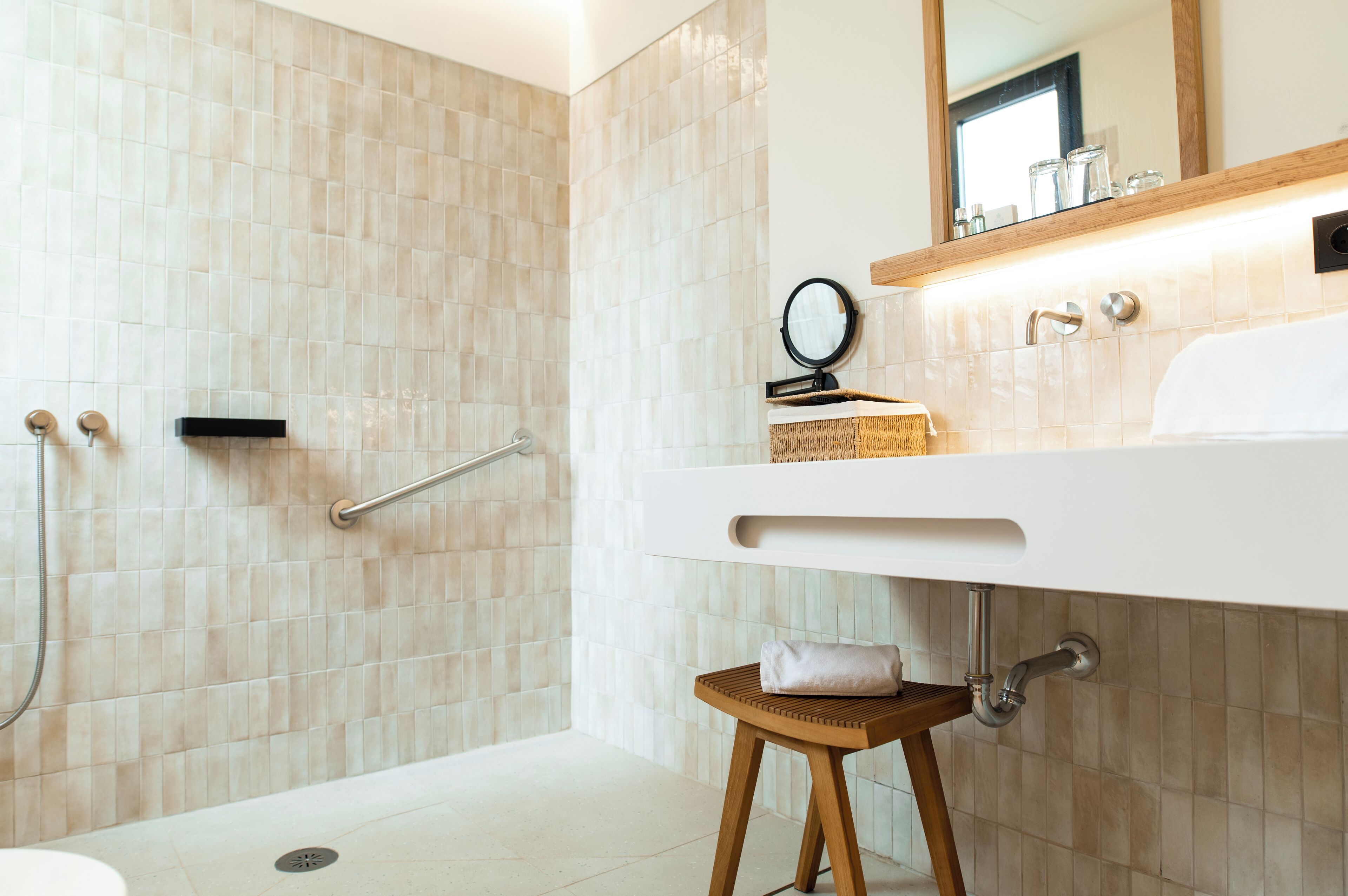 Une salle de bain moderne avec une douche, un lavabo avec un miroir et un petit tabouret.
