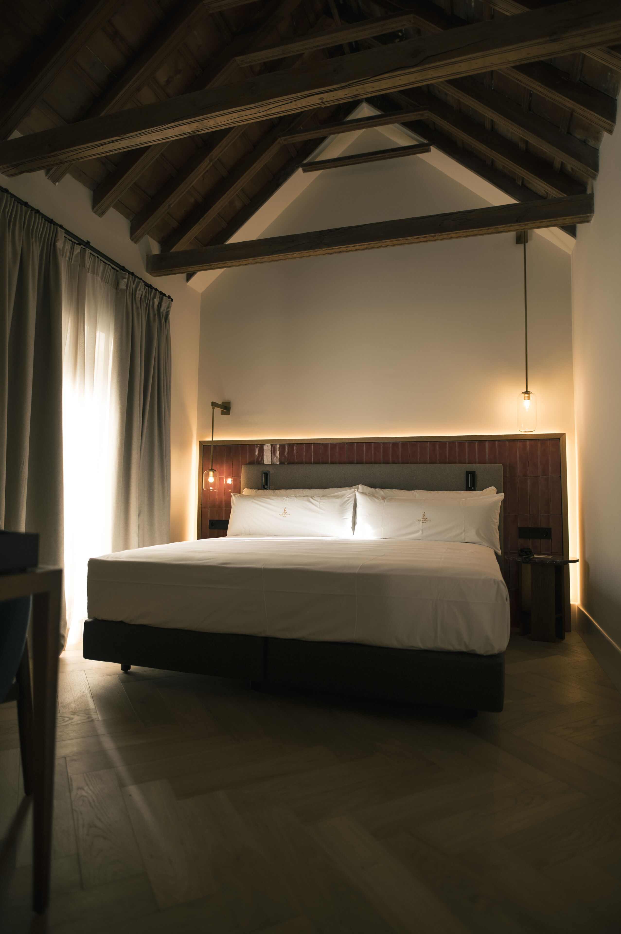 Una camera da letto con un letto grande, travi in legno a soffitto, un comodino e una lampada.