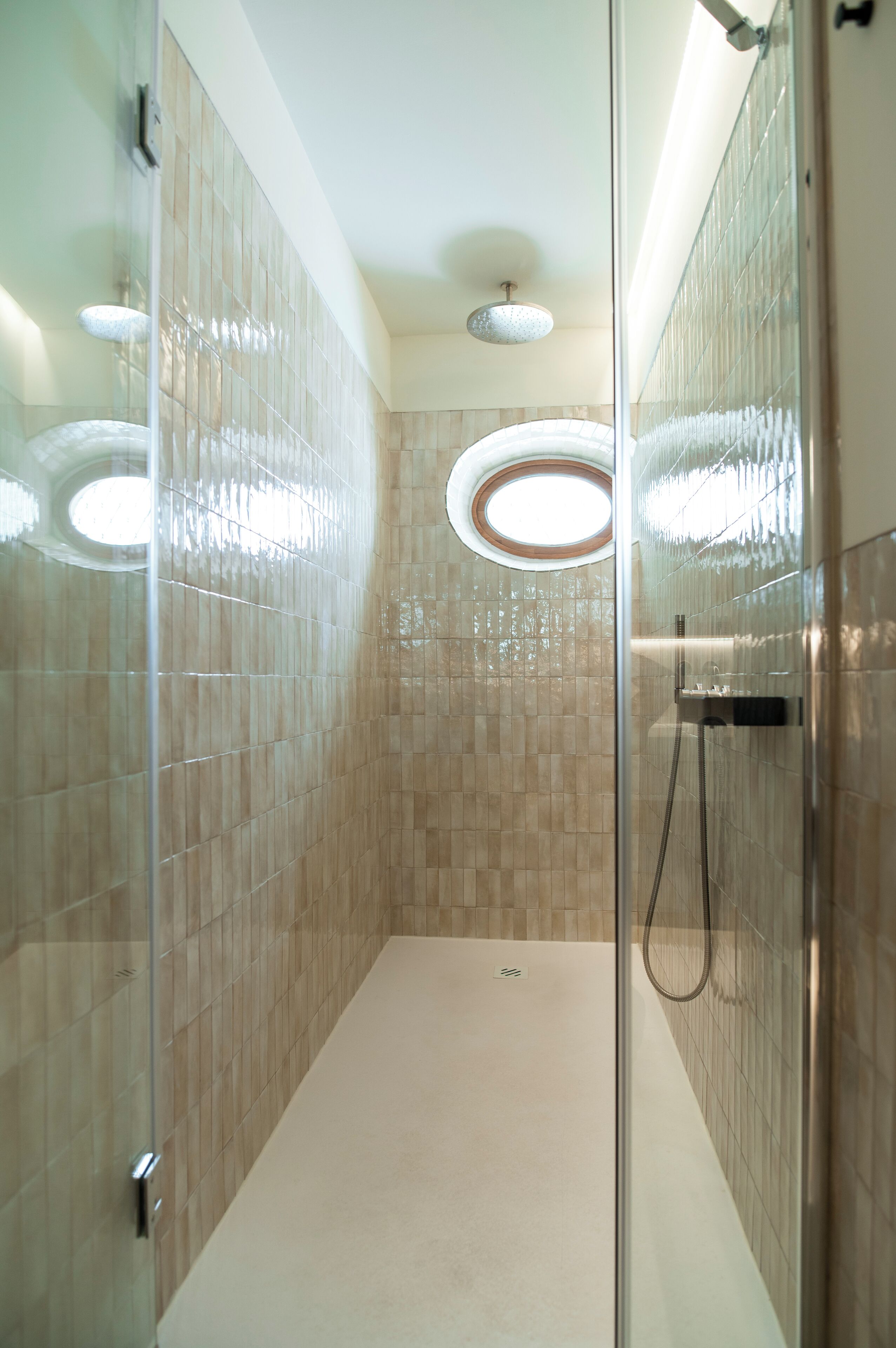 A glass-enclosed shower with beige tiles and a circular skylight.