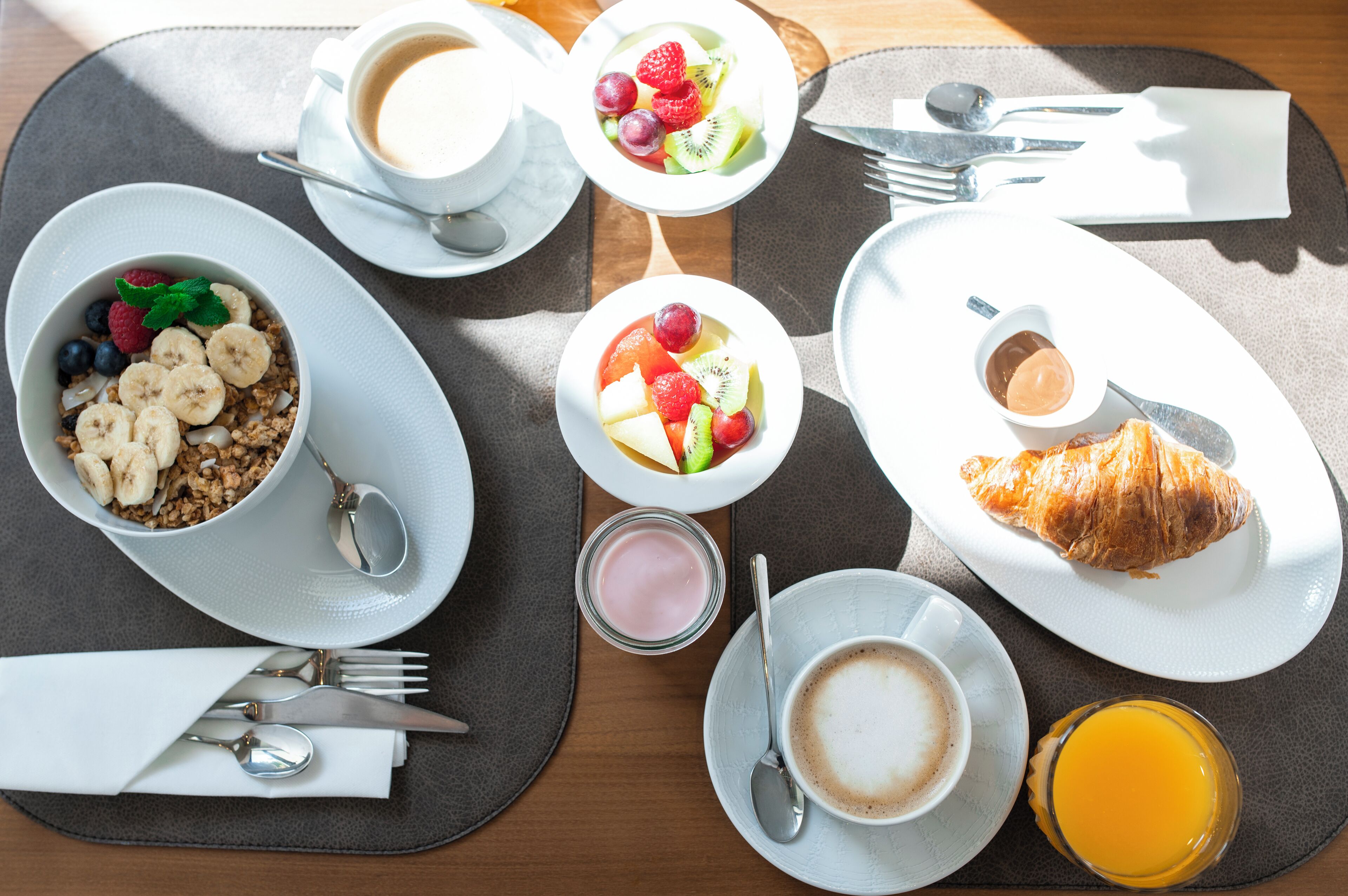 A breakfast setting with various dishes including cereal, fruit, croissant, coffee, and juice.