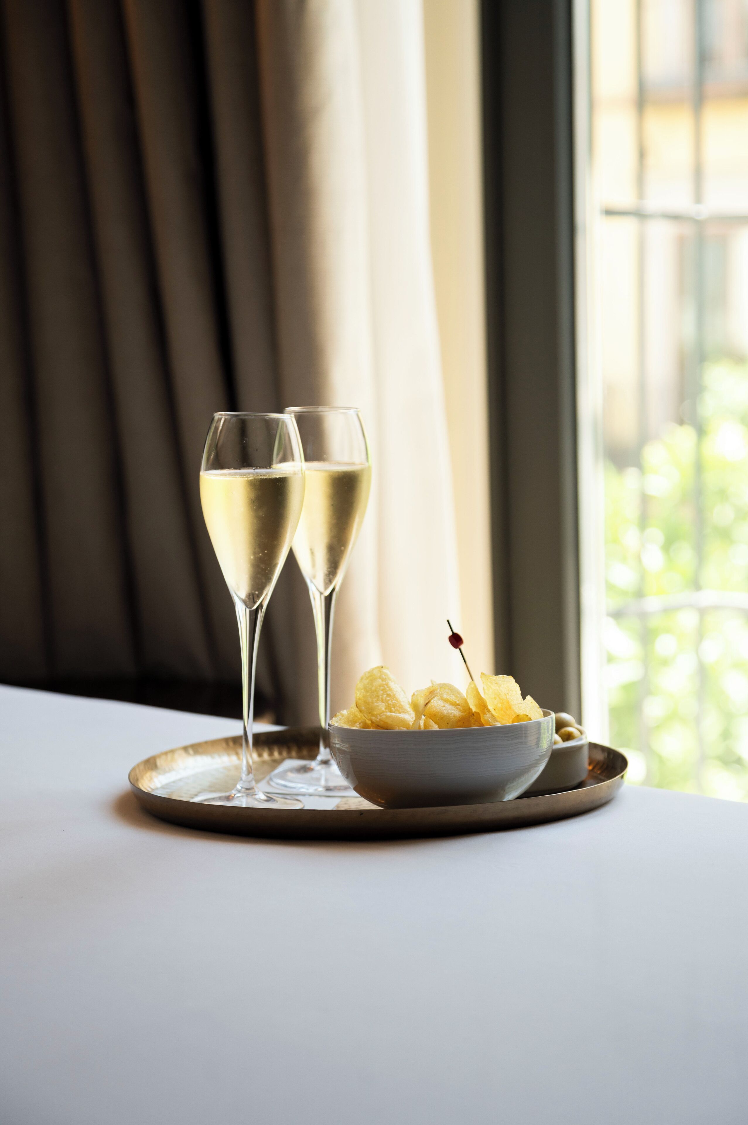 Two glasses of champagne on a tray with a bowl of chips.
