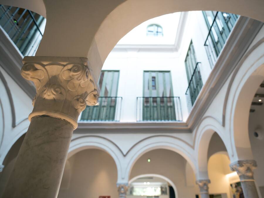 Une colonne de marbre surmontée d’une tête sculptée, dans un bâtiment doté de voûtes en arc et de balcons.