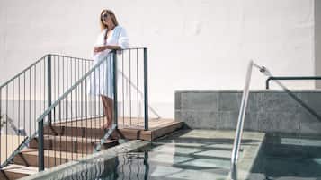 Una persona de pie sobre una terraza de madera junto a una piscina con barandillas metálicas.