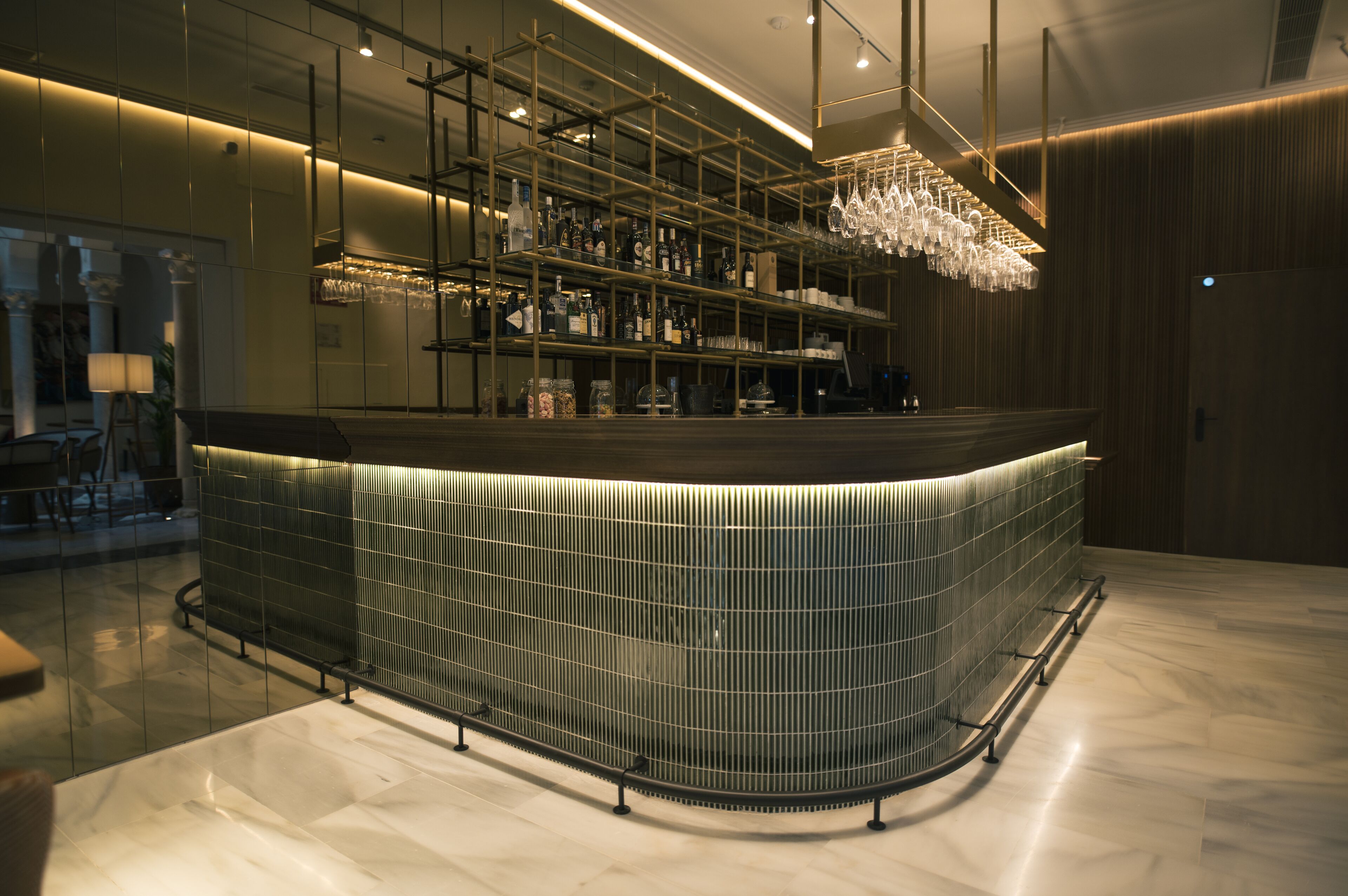 A modern bar area with a curved counter, shelves with bottles, and a hanging light fixture.