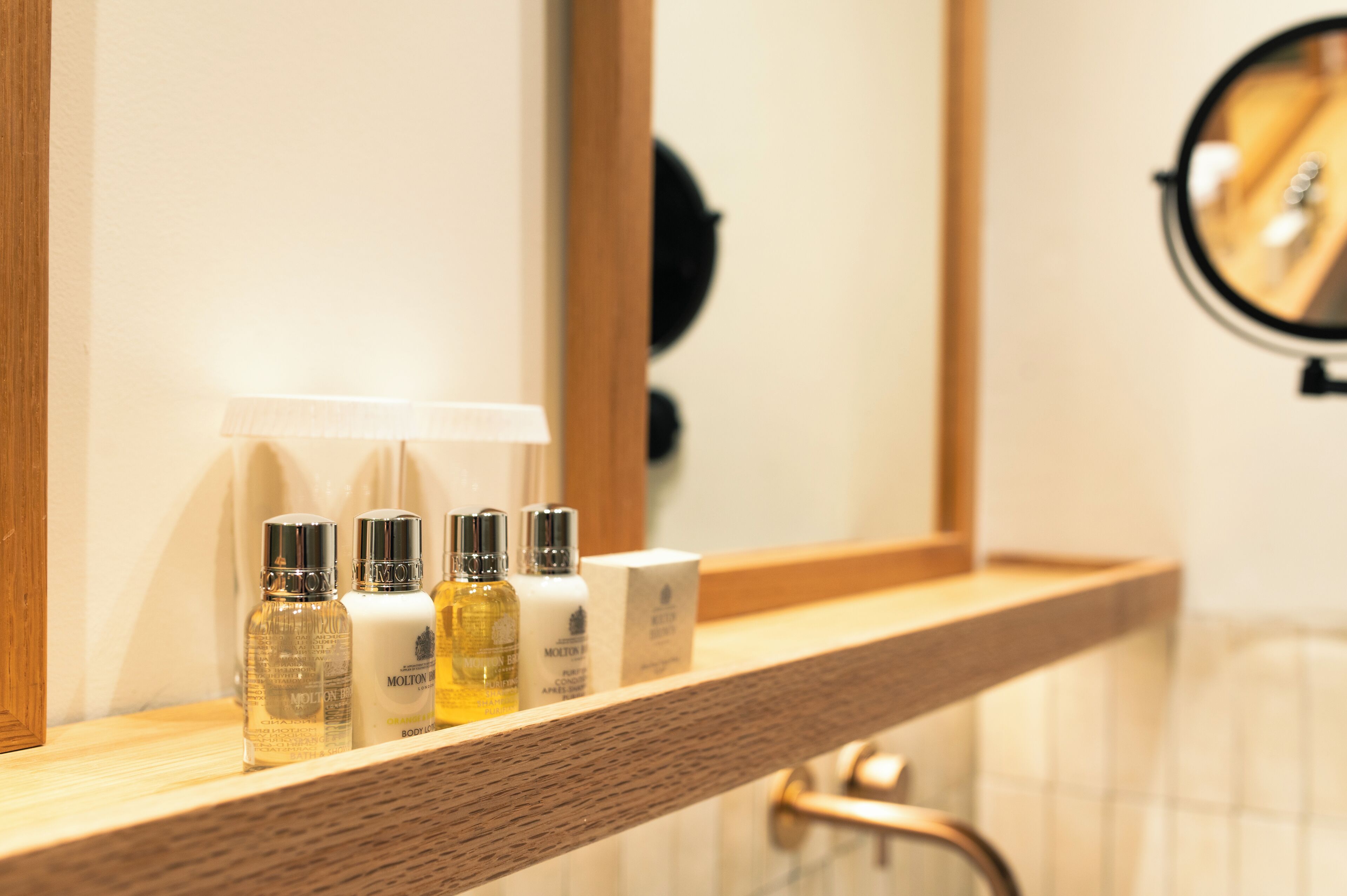 A bathroom vanity with a mirror, a wooden shelf, and three bottles of toiletries.