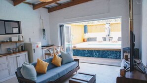 Una sala de estar acogedora con sofá, vigas de madera, zona de cocina y vistas a una piscina al aire libre.