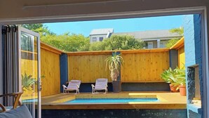 Un patio moderno al aire libre con piscina, terraza de madera y sillones de descanso.