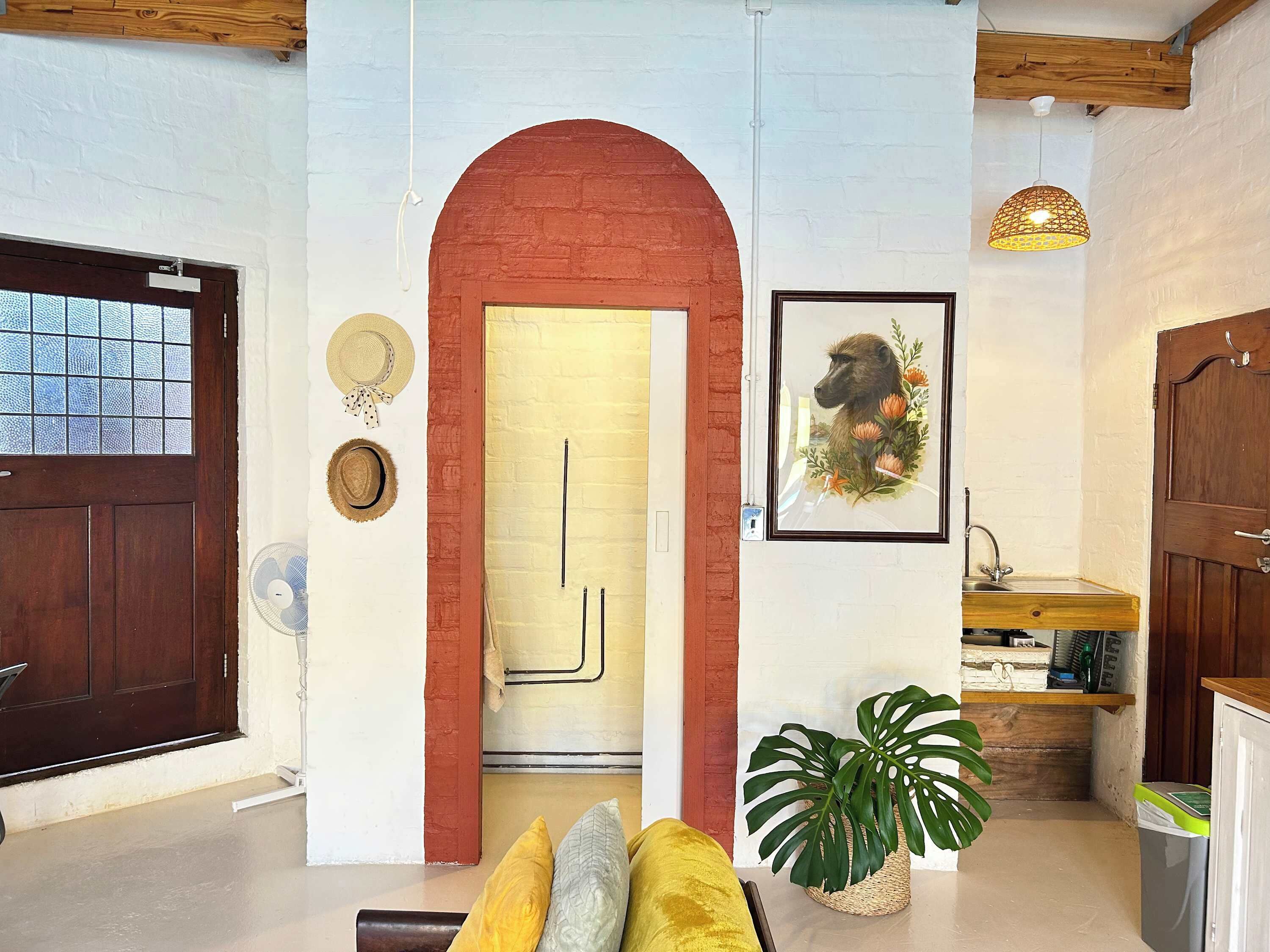 A room with a wooden door, a red archway, a framed picture, a plant, and a small sink area.