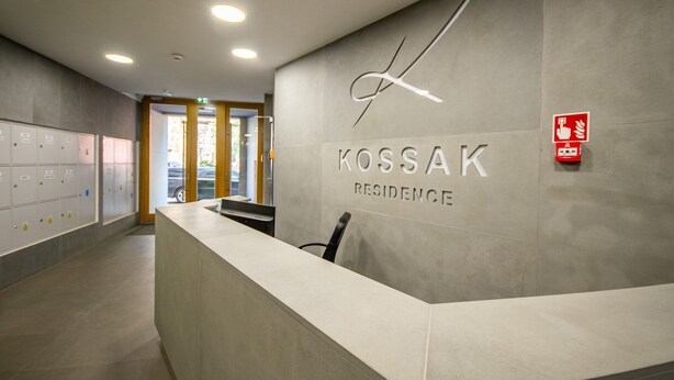 Vastaanottotiski, jossa on kyltti, jossa lukee ”KOSSAK RESIDENCE”, ja seinällä palovaroitin.
