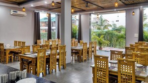 A restaurant with wooden tables and chairs, large windows, and hanging pendant lights.