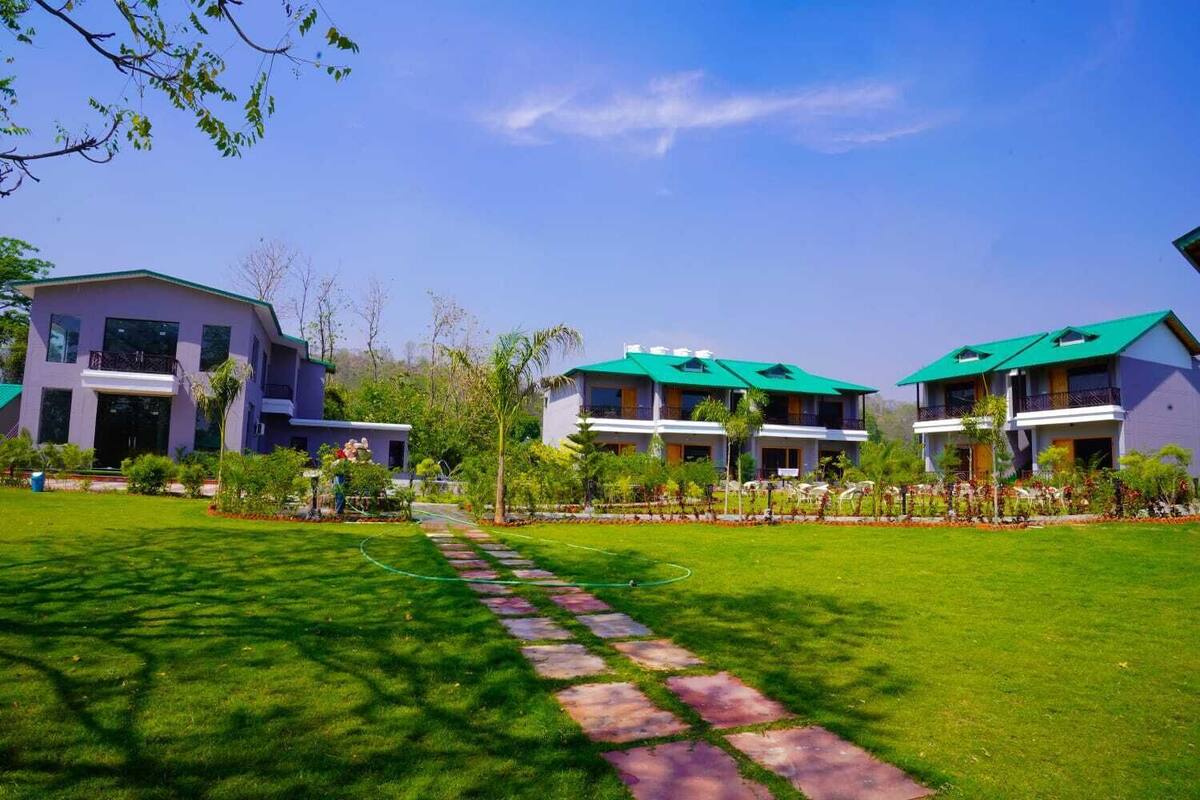 A hotel with three buildings, each with a green roof and multiple balconies. There is a well-maintained lawn with a stone pathway leading to the entrance.