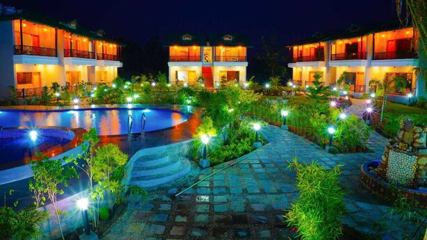 A hotel with a swimming pool, outdoor lighting, and lush greenery.