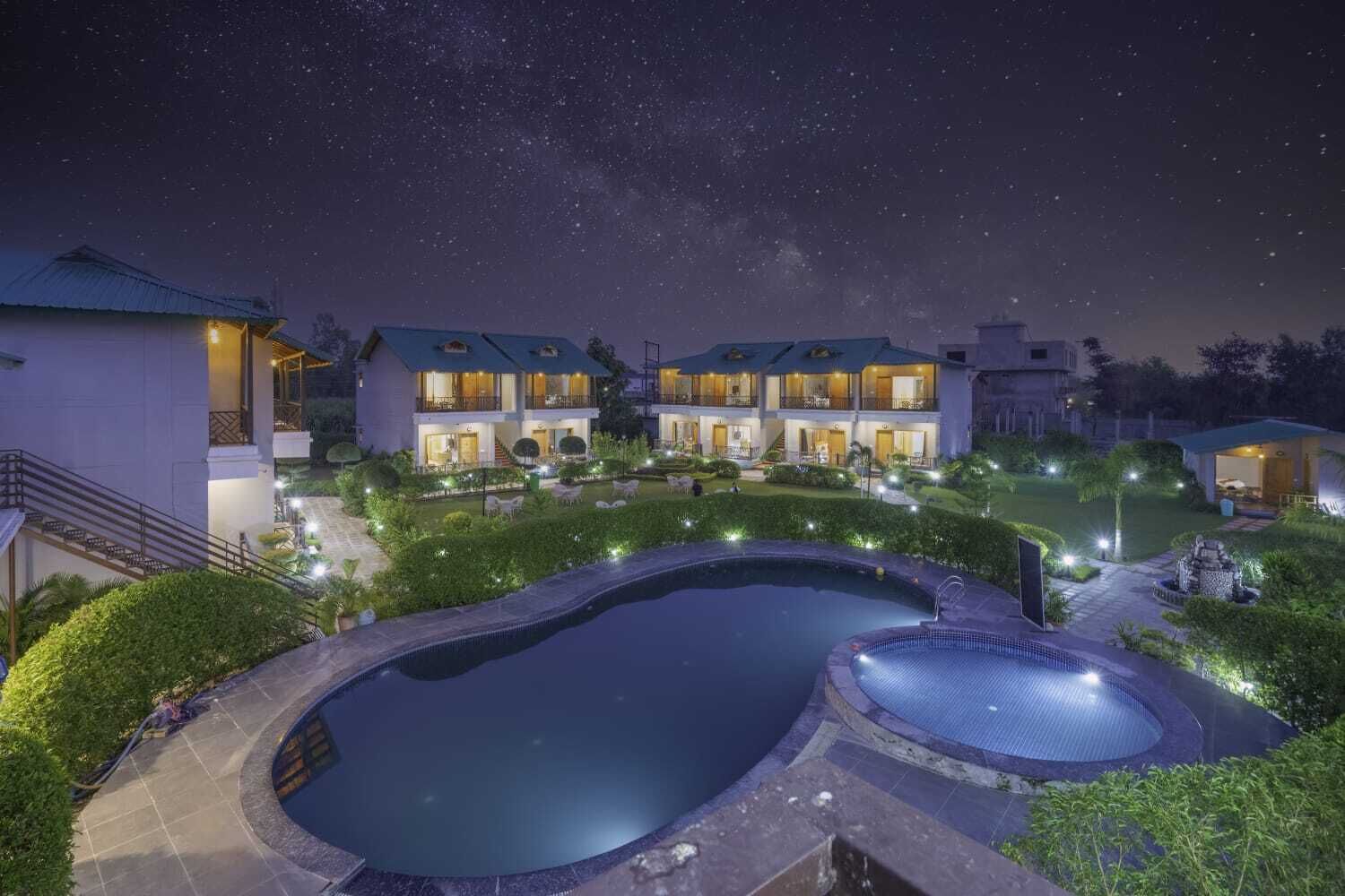 Um resort com piscina, vários quartos de hóspedes e área externa bem iluminada à noite.