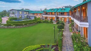 A multi-story hotel with a green roof, a well-maintained lawn, and a stone pathway leading to the entrance.