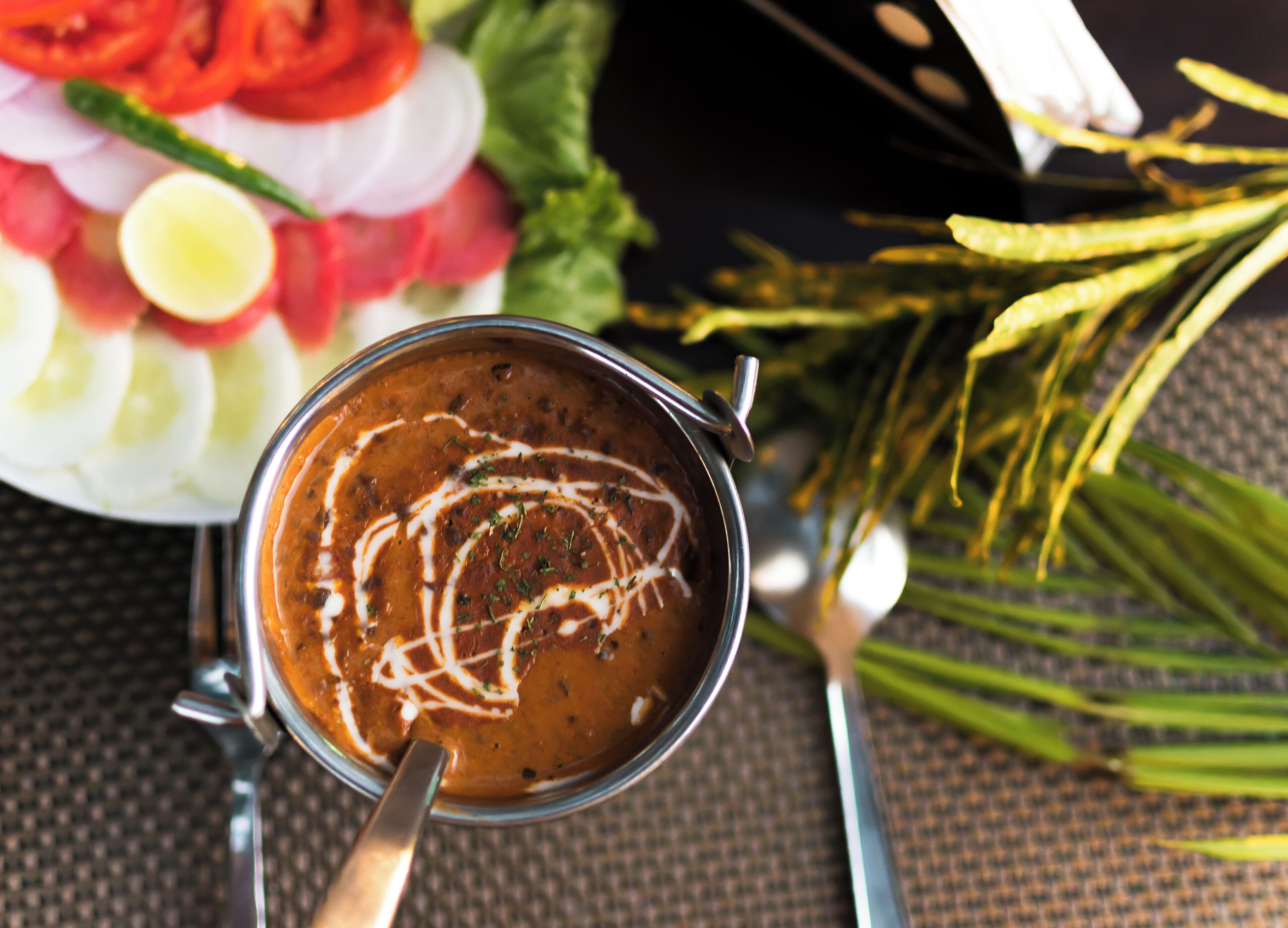 Un bol de soupe avec une cuillère, entouré de légumes et d’herbes aromatiques.