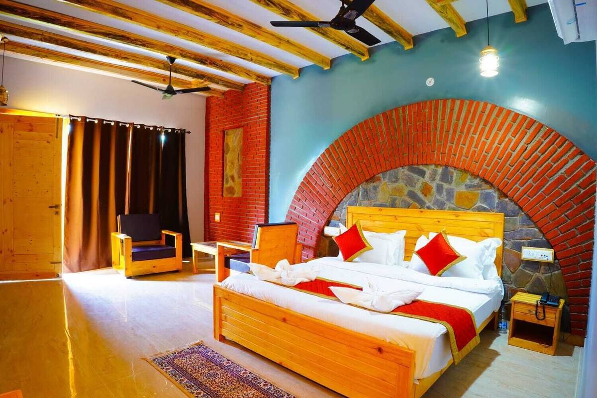 A bedroom with a wooden bed, a chair, a small table, and a stone wall arch.