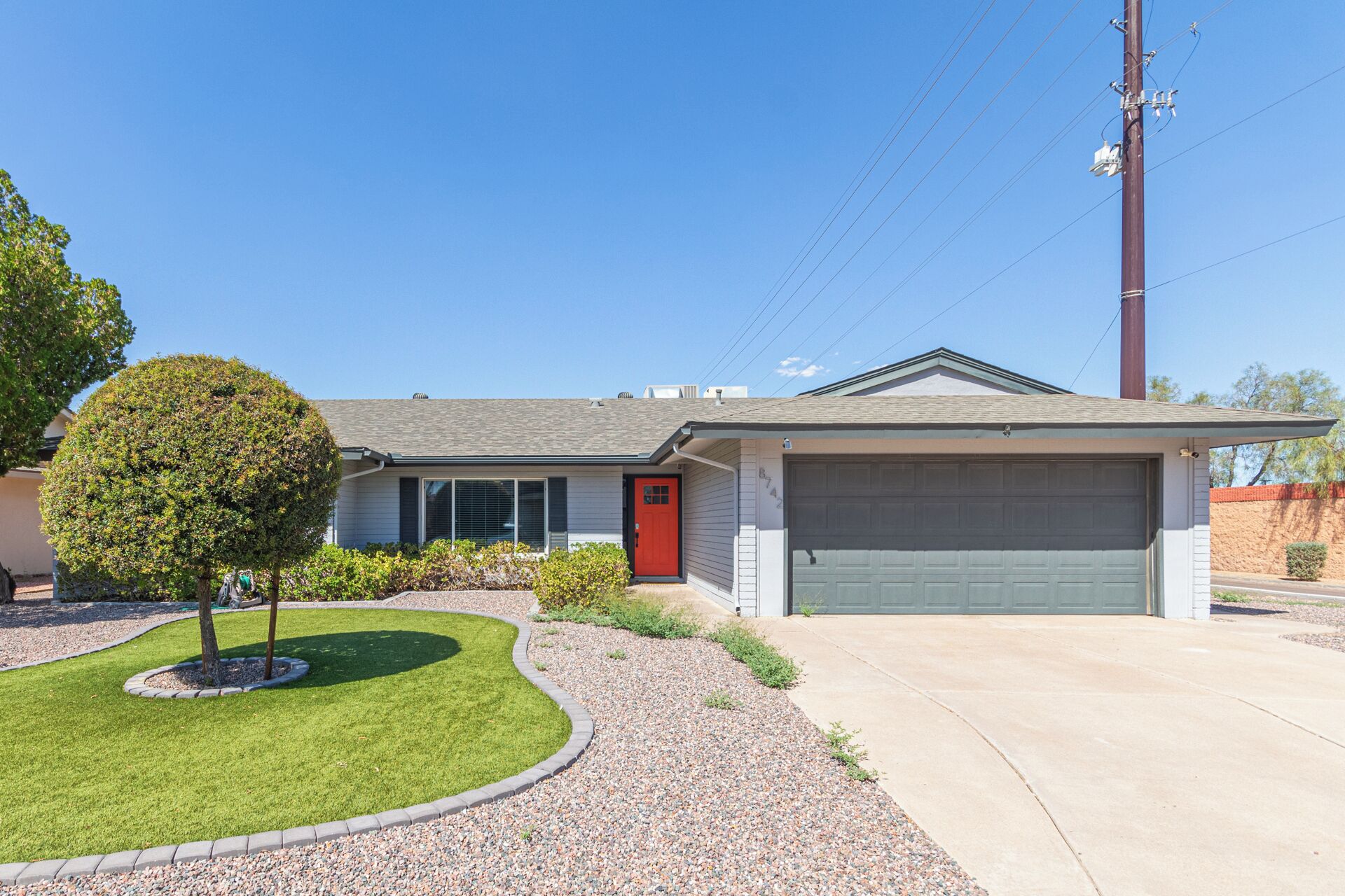 A single-story house with a red door, a garage, and a well-maintained lawn.