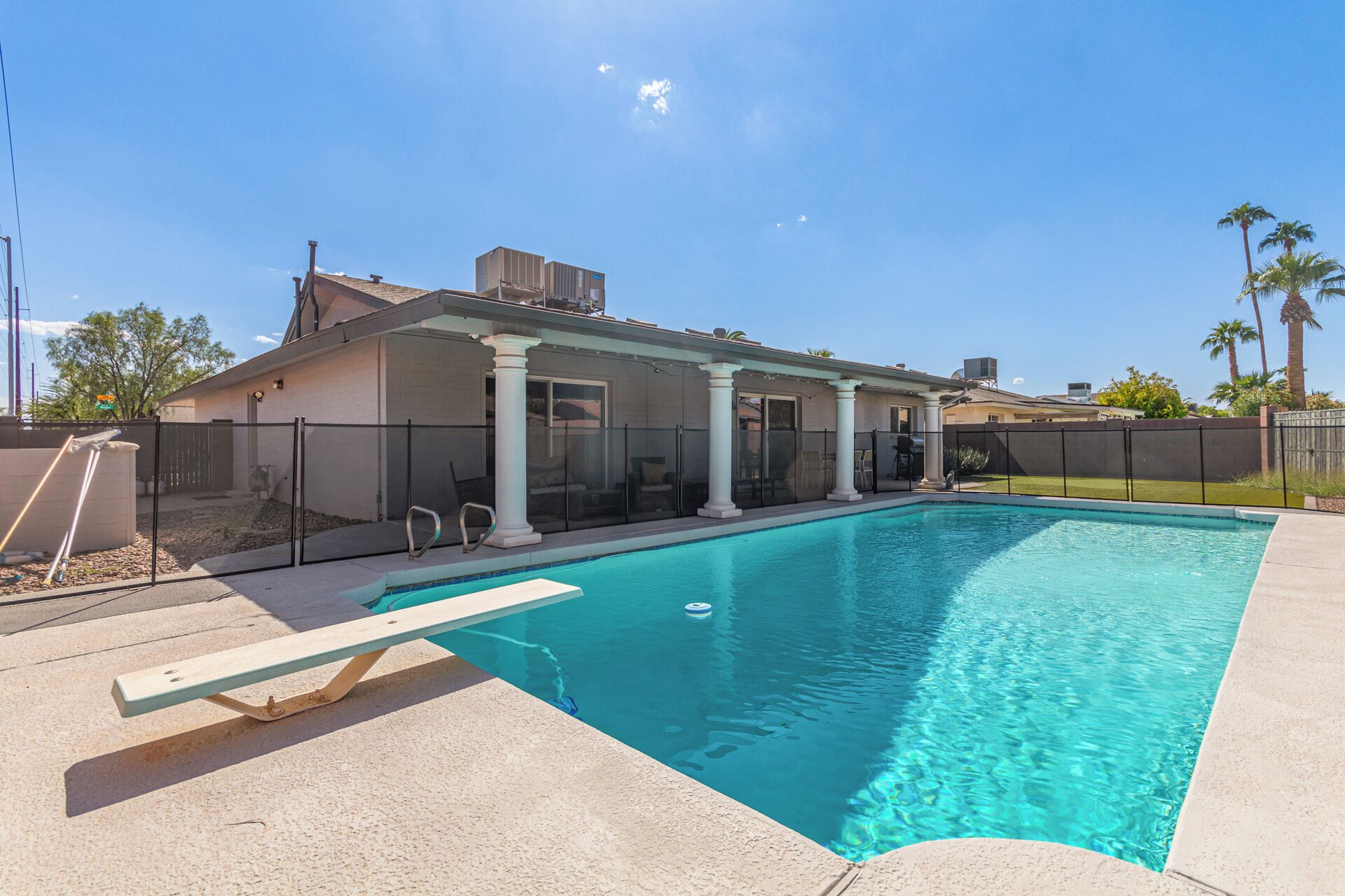 Une piscine avec un patio couvert, une cour clôturée et des palmiers en arrière-plan.