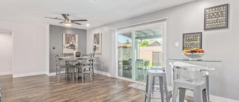 A spacious kitchen with a dining area, a sliding glass door leading to a backyard, and a bar area with stools.