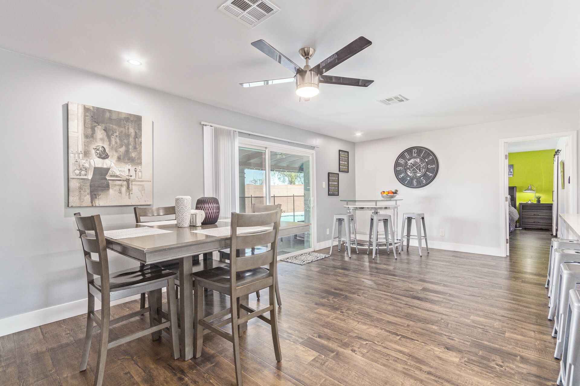 A spacious dining area with a wooden table and chairs, a ceiling fan, and a large wall clock.
