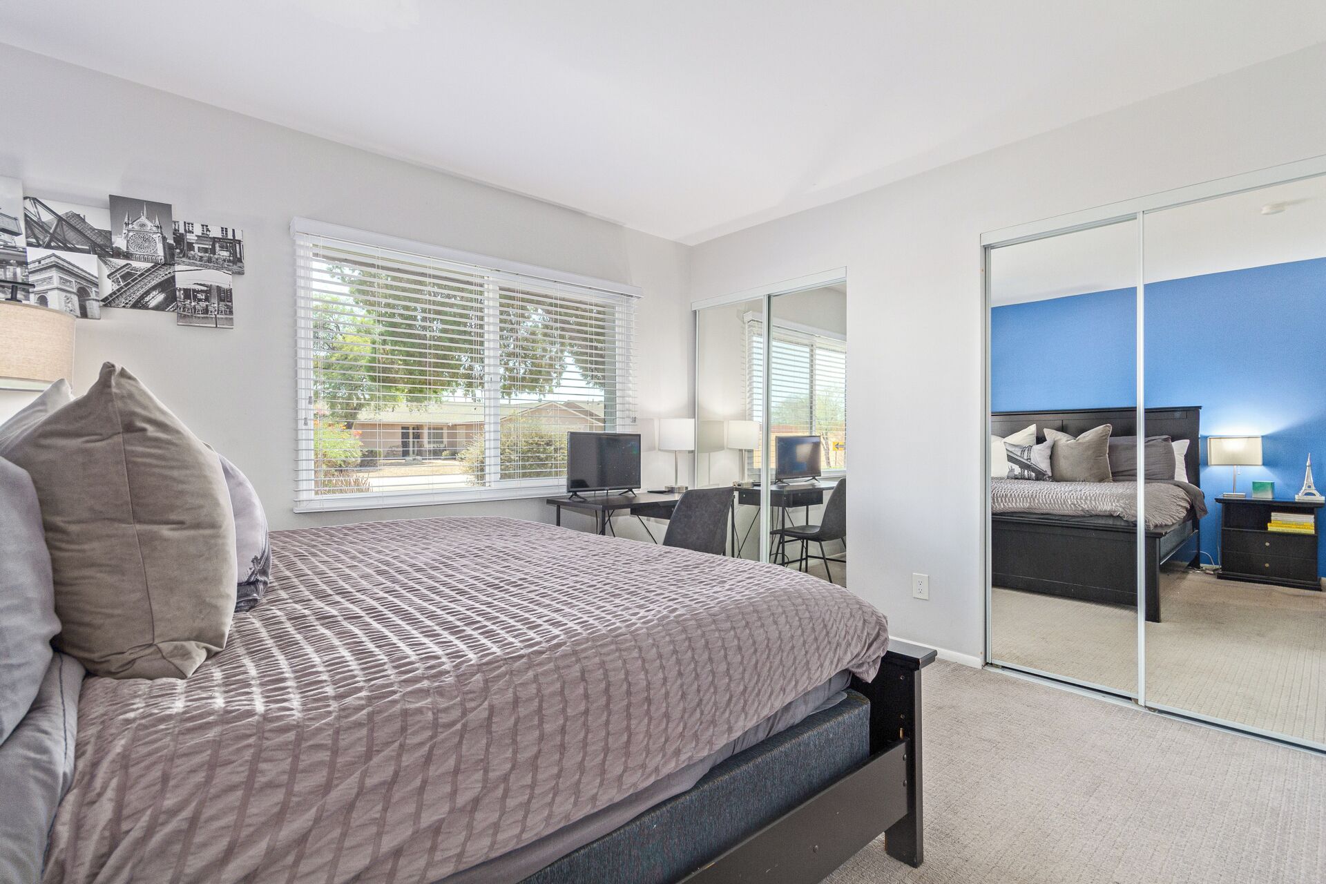 A bedroom with a bed, a desk, a computer, and a large mirror.