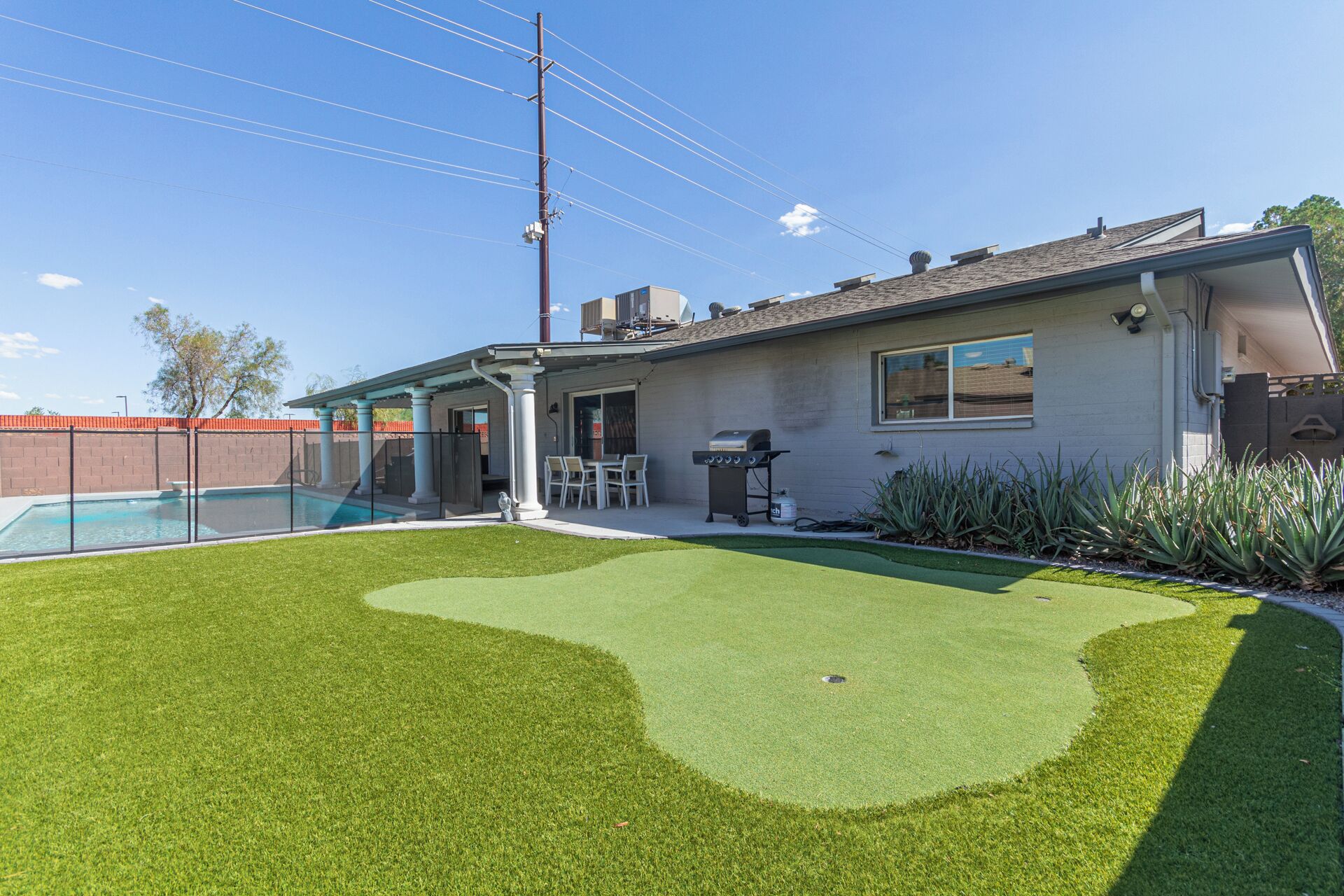 Un patio trasero residencial con piscina, césped artificial y zona de barbacoa.