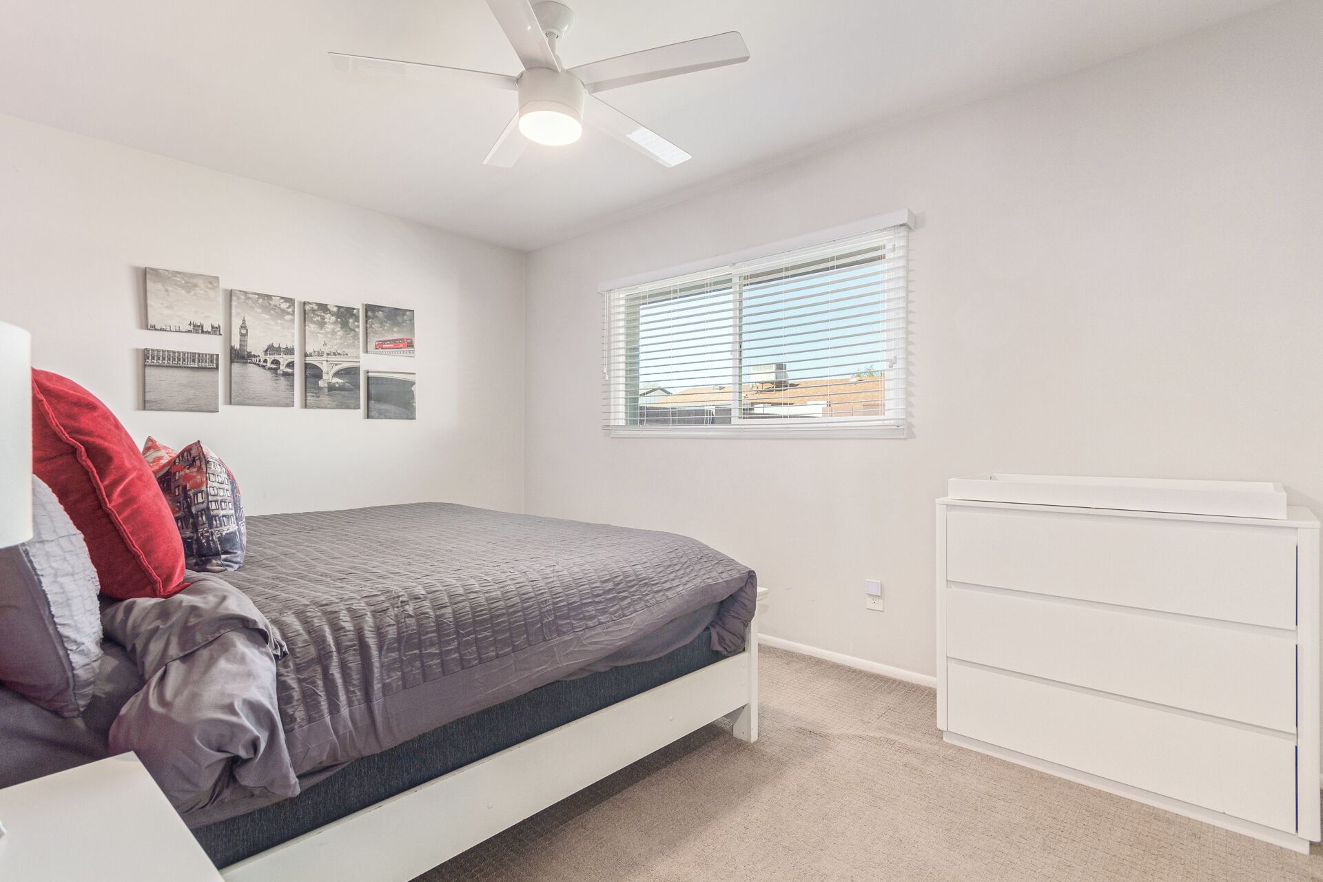 A bedroom with a bed, a ceiling fan, a window with blinds, and a dresser.