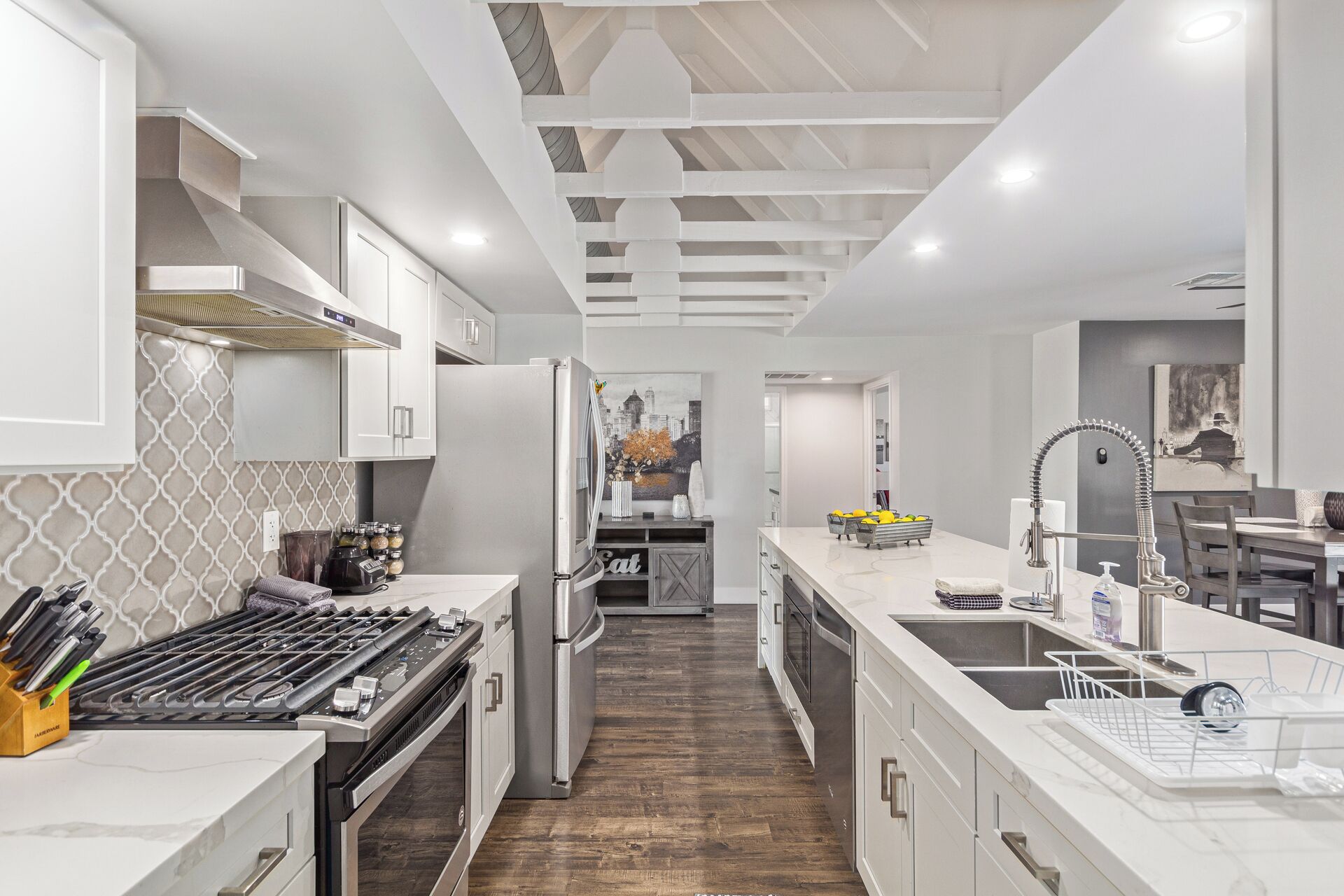 A modern kitchen with white cabinetry, stainless steel appliances, and a wooden floor.