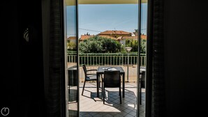 Uma varanda com mesa e cadeiras, vista para um edifício com telhado de azulejos e cerca verde.