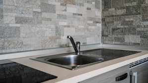 Cozinha com pia de aço inoxidável, bancada preta e backsplash revestido com azulejos.