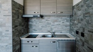 Cocina compacta con dos fregaderos, una campana extractora de acero inoxidable y lavavajillas integrado. El salpicadero está hecho con baldosas de piedra gris, y los armarios tienen un acabado de madera clara.