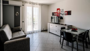 Quarto moderno e bem iluminado, com sofá, mesa de jantar com cadeiras, televisão e área de cozinha.