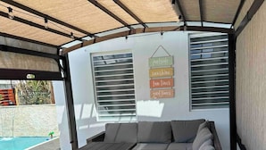 A covered outdoor seating area with a pool in the background.