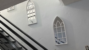 A staircase with a black handrail and white walls. There are two windows with decorative designs on the wall.