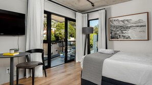 Ein modernes Hotelzimmer mit einem großen Bett, einem Flachbildfernseher, einem Esstisch mit Stühlen und einem Balkon mit Blick auf Stadt und Berge.