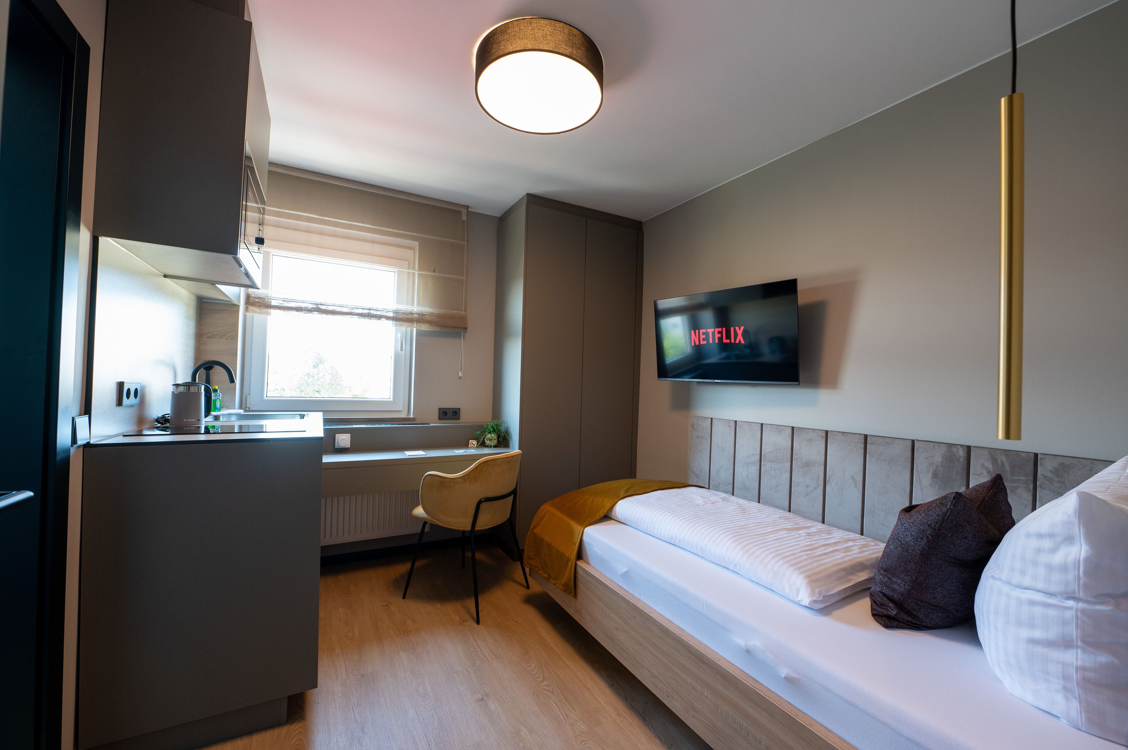 A modern hotel room with a bed, a desk, a chair, a TV, and a window.