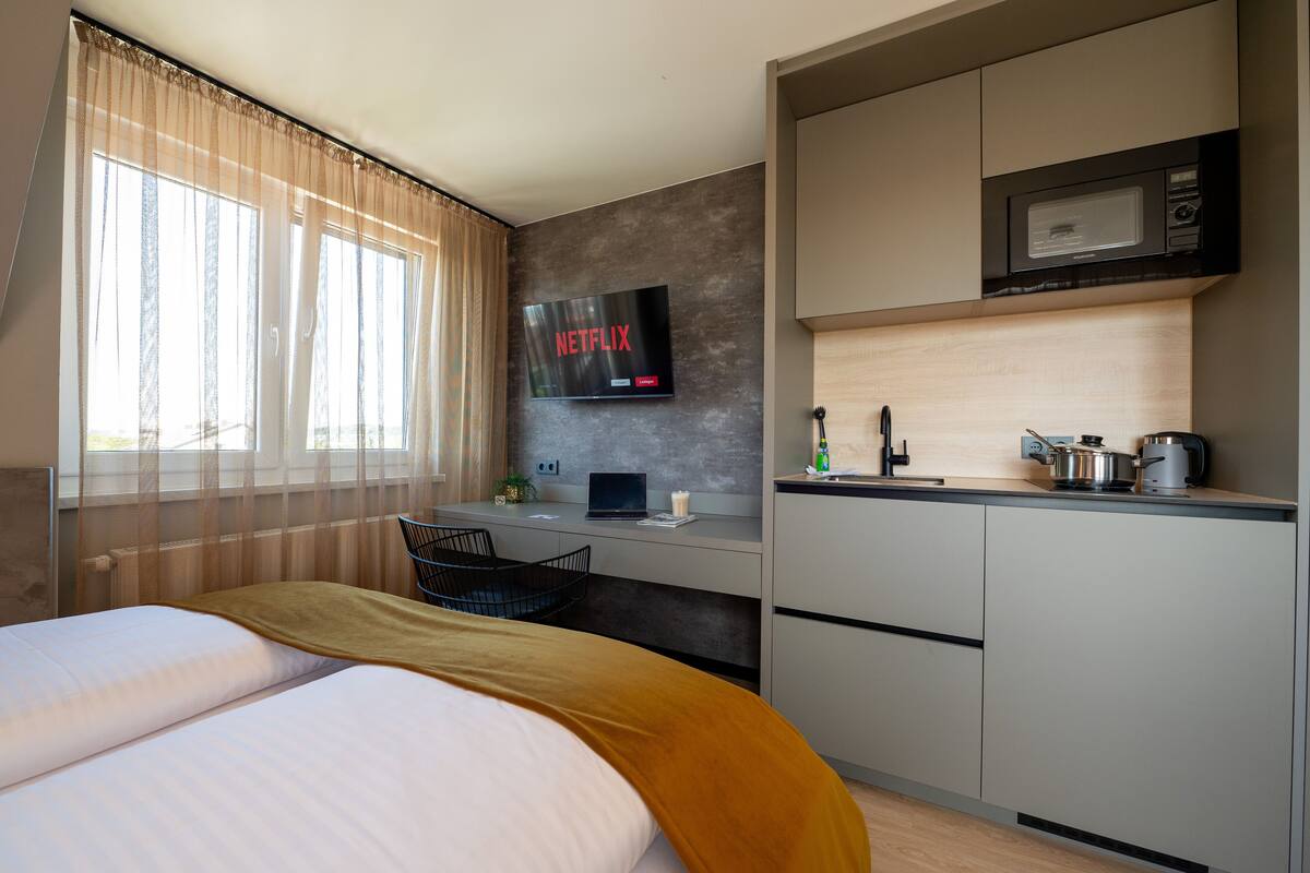 A hotel room with a bed, a desk with a laptop, a microwave, and a TV displaying Netflix.