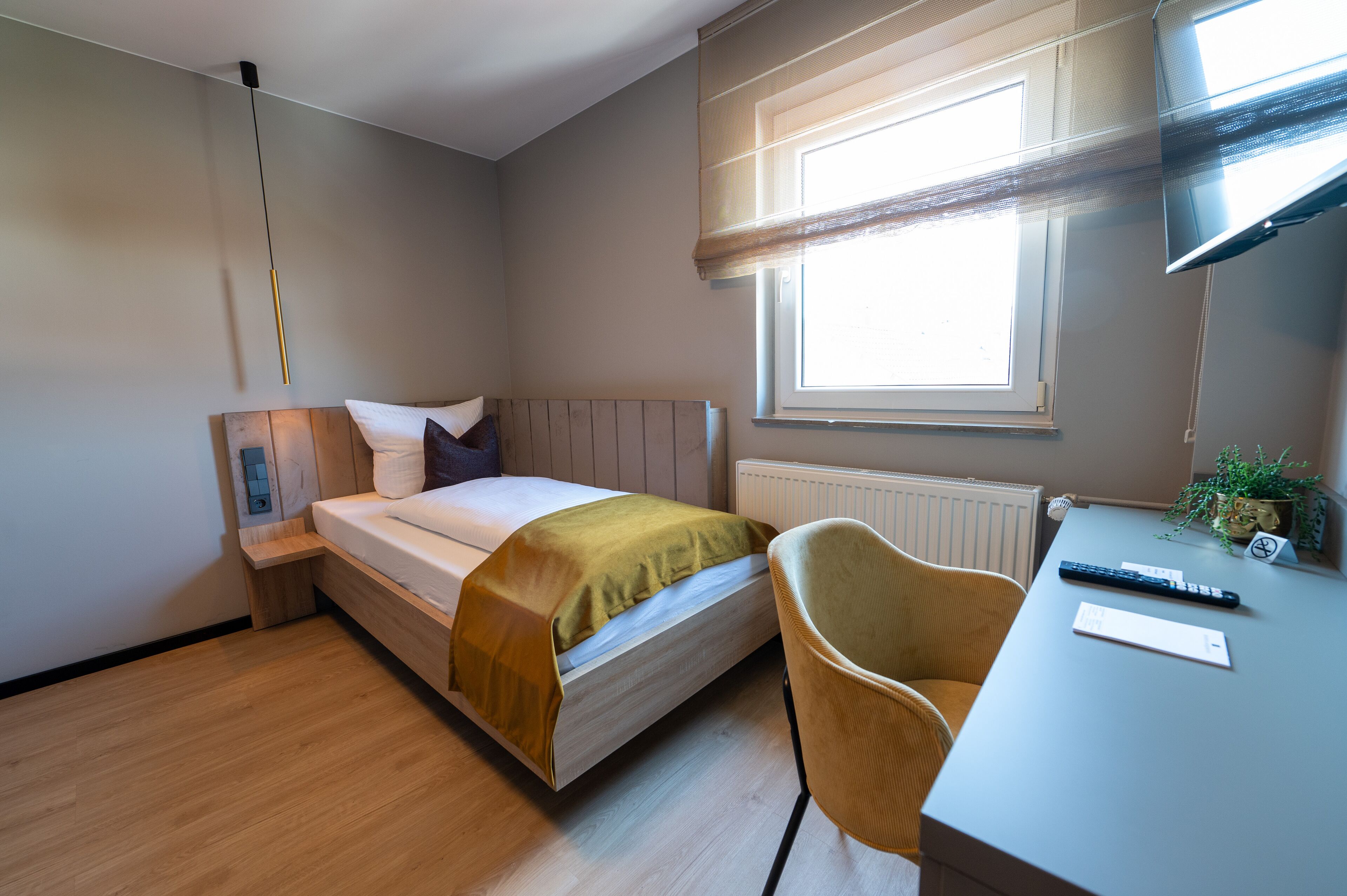 A bedroom with a bed, bedside table, chair, and a window with blinds.