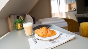 Aamiaispöytä, jossa on croissant, lasillinen kahvia ja sanomalehti.