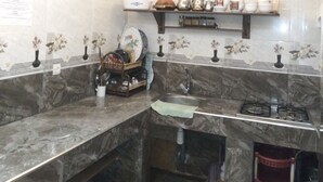 A kitchen with marble countertops, a gas stove, and a sink. There are shelves with kitchenware and a hanging light fixture.
