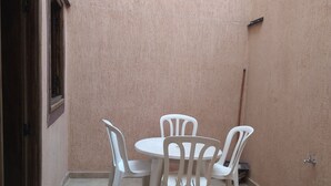 A small patio with a round table and four white plastic chairs, surrounded by a textured pink wall and a tiled floor.
